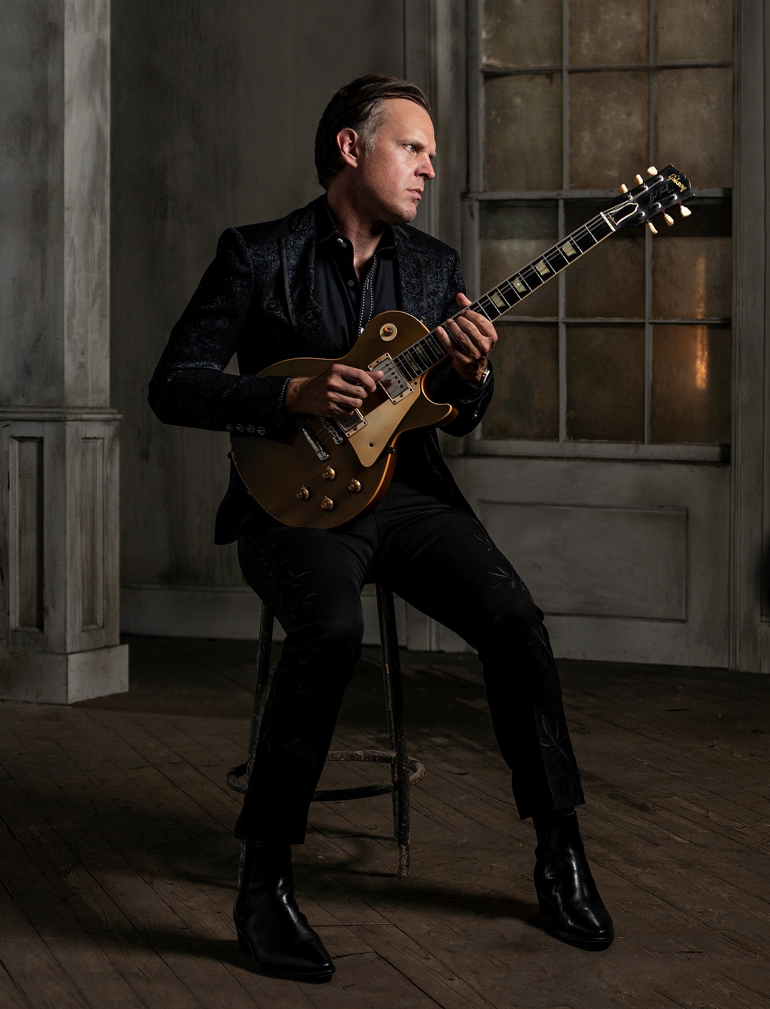 Joe Bonamassa sitting on a stool in an old mansion holding a Les Paul.